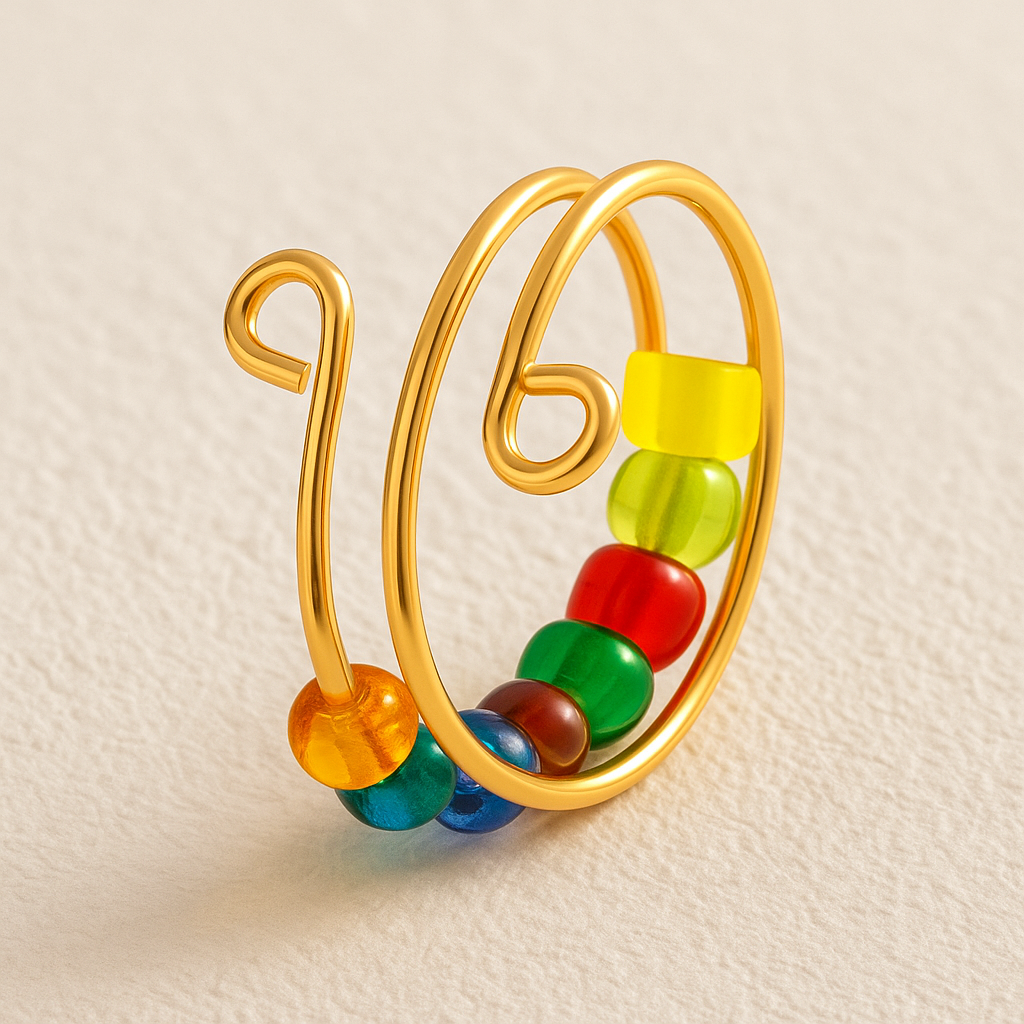 The Adjustable Beaded Crochet & Anxiety Relief Tool features a gold wire spiral ring with colorful round beads in yellow, orange, green, red, and blue—an elegant yarn tension ring that also aids anxiety relief on a textured light beige surface.